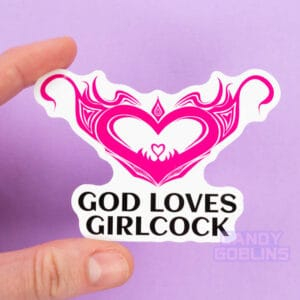 A person holds a sticker of a hot pink womb heart design. The text underneath reads "god loves girlcock"