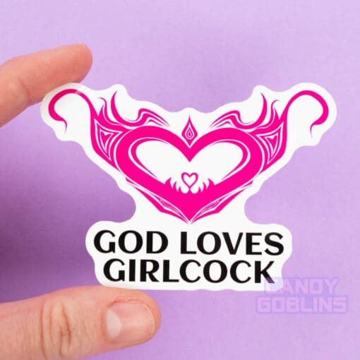 A person holds a sticker of a hot pink womb heart design. The text underneath reads "god loves girlcock"
