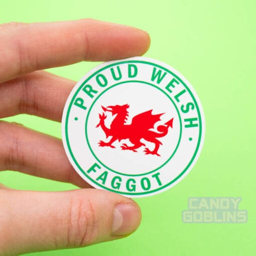 A person holds up a circle sticker with a Welsh dragon in the middle, text around it reads "Proud Welsh Faggot"