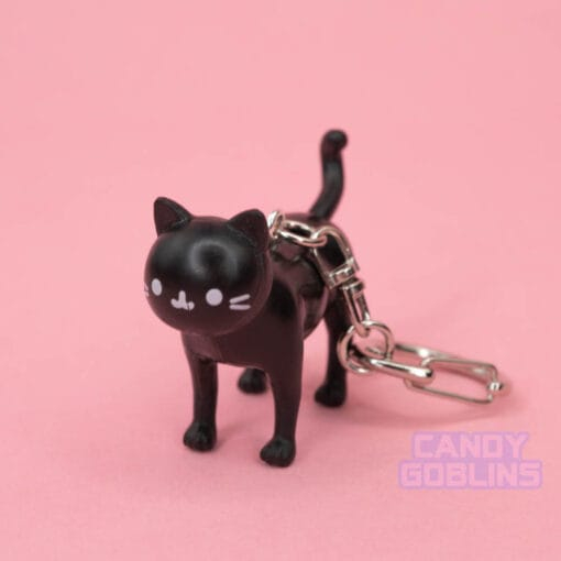 A black cat keychain looks at the camera, with a content expression on it's face