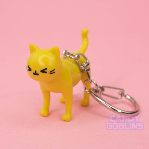 A yellow cat keychain looks at the camera with an excitedly happy expression