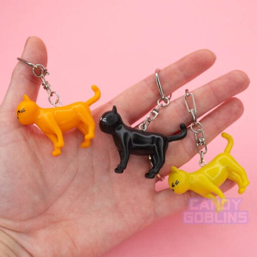 A person holds three different coloured cat keychains