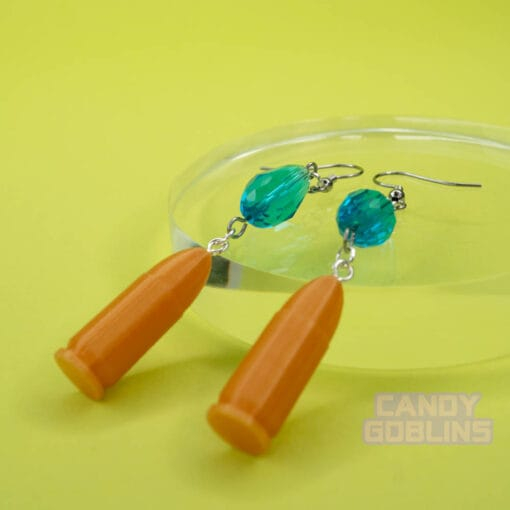 A pair of our Revolver Earrings lie against a photo prop. They're angled away from the camera so you can see the details of the bullets