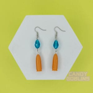 A pair of our Revolver Earrings lie against a photo prop. You can clearly see the replica bullet design, and blue bead