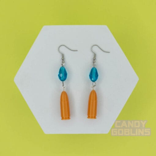 A pair of our Revolver Earrings lie against a photo prop. You can clearly see the replica bullet design, and blue bead