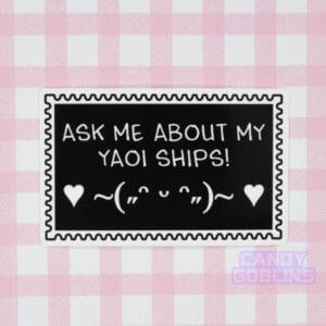 A stamp shaped sticker reads: Ask Me About My Yaoi Ships. Under the text is a happy emoticon, blushing and dancing with hearts. It's against a pink background.