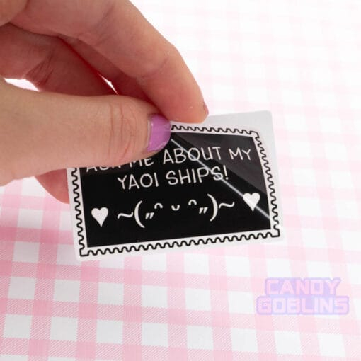 A action shot of someone peeling our "Ask me about my yaoi ships sticker". The surface of the sticker is super shiny!