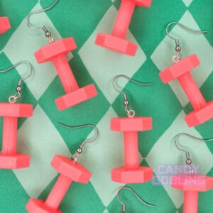 Many pink dumbbell earrings are scattered against a green diamond print backdrop