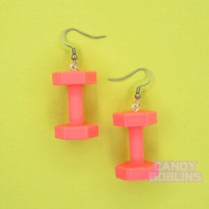 A pair of bright pink dumbbell earrings lay against a green background