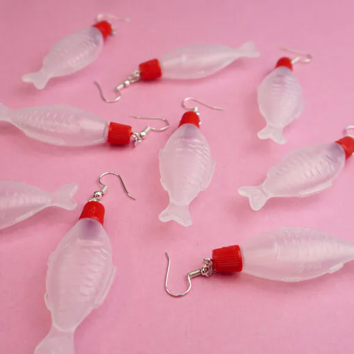 A bunch of different soy sauce earrings are scattered across a pink backdrop. They all point in different directions