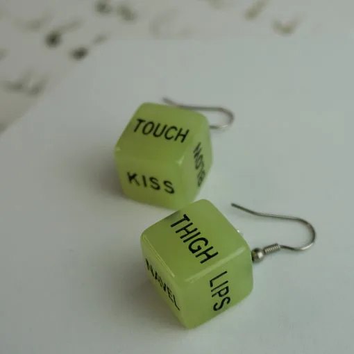 A pair of our glow in the dark sex dice earrings. They say the words "touch" and "thigh". The words "lips" and "kiss" can also be seen on another side of them.