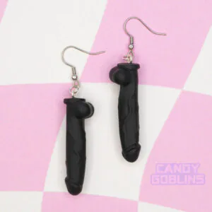 A pair of black dildo earrings against a pink and cream background.