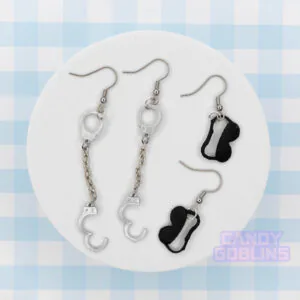 Handcuff and eye mask earrings sit next to each other on a photo prop