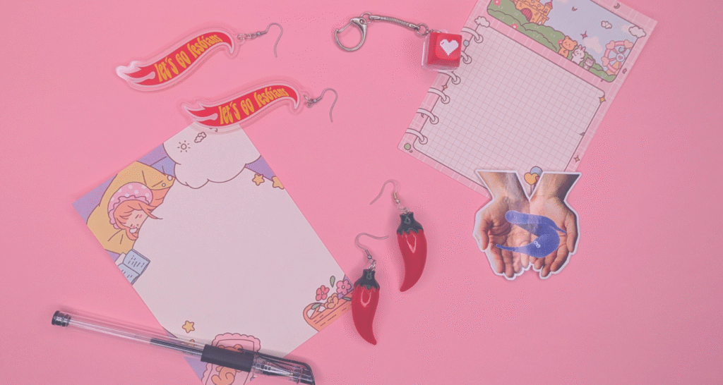 Note paper, pens, earrings, and keychains are scattered against a pink backdrop.